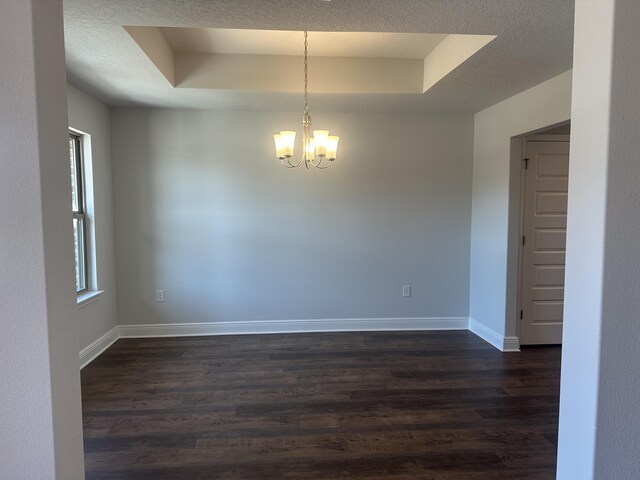 unfurnished room featuring a raised ceiling, dark wood finished floors, baseboards, and an inviting chandelier