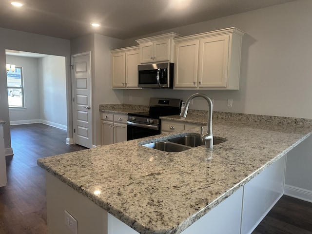 kitchen featuring appliances with stainless steel finishes, a peninsula, light stone countertops, white cabinetry, and a sink