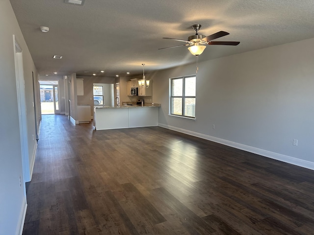 unfurnished living room with dark wood-type flooring, a ceiling fan, a sink, a textured ceiling, and baseboards