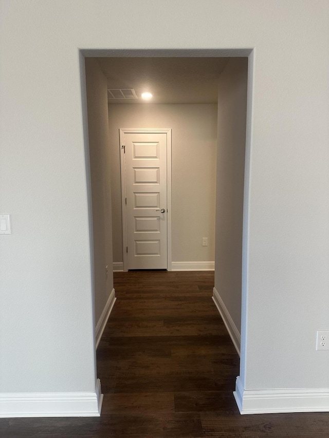 hallway with dark wood-style floors, visible vents, and baseboards