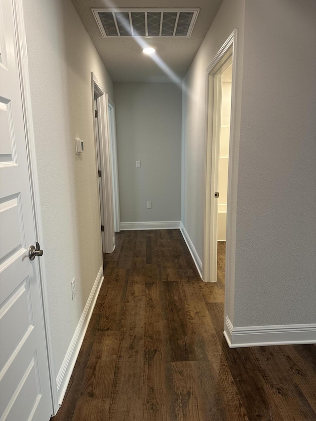 hallway featuring dark wood-style floors, baseboards, and visible vents