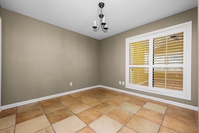 spare room featuring a notable chandelier, a textured ceiling, and light tile patterned floors