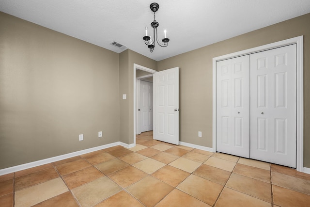 unfurnished bedroom with a closet, a notable chandelier, and light tile patterned floors