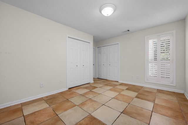 unfurnished bedroom featuring light tile patterned flooring and multiple closets