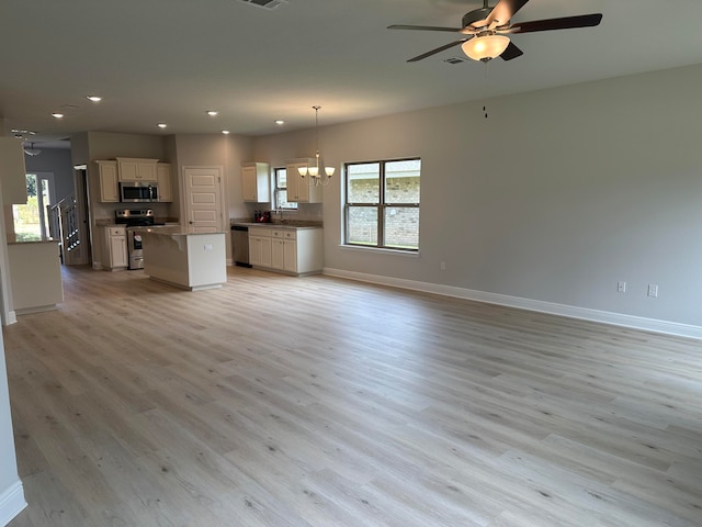 unfurnished living room featuring sink, light wood-type flooring, and ceiling fan with notable chandelier