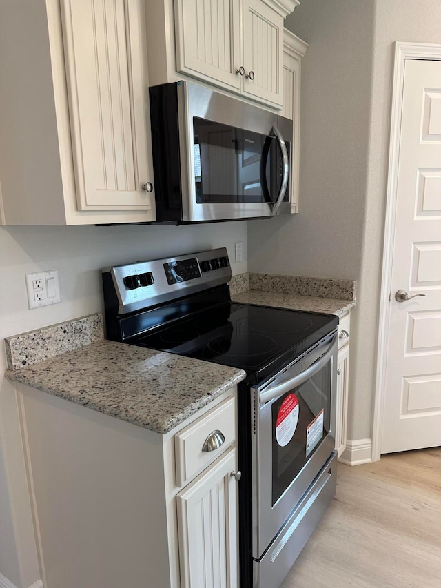 kitchen with appliances with stainless steel finishes, light wood-type flooring, and light stone counters