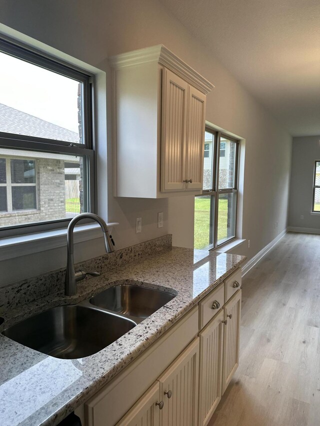 kitchen featuring light brown cabinetry, sink, light wood-type flooring, and light stone countertops