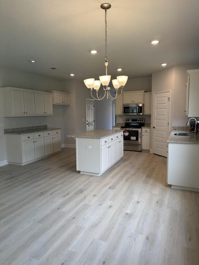 kitchen with appliances with stainless steel finishes, white cabinets, sink, pendant lighting, and light wood-type flooring