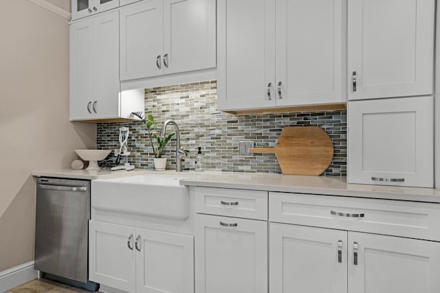 kitchen featuring light countertops, decorative backsplash, stainless steel dishwasher, white cabinetry, and a sink