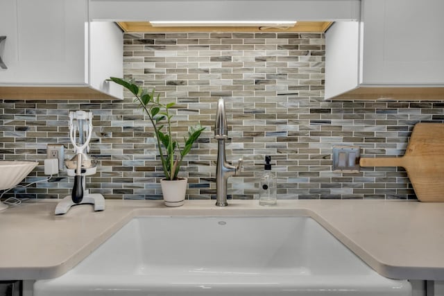 interior details featuring tasteful backsplash, white cabinetry, light countertops, and a sink