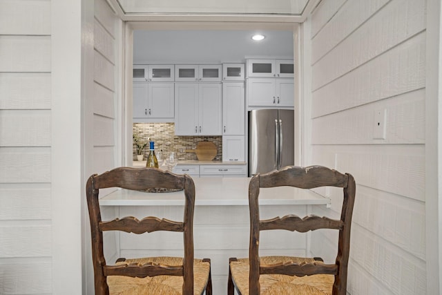 kitchen with white cabinets, light countertops, freestanding refrigerator, tasteful backsplash, and glass insert cabinets