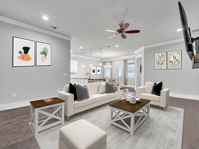 living room with wood-type flooring, sink, ornamental molding, and ceiling fan with notable chandelier