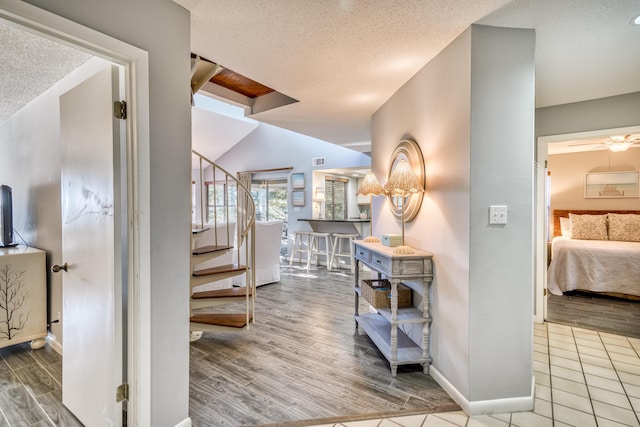 hall featuring lofted ceiling, light hardwood / wood-style flooring, and a textured ceiling