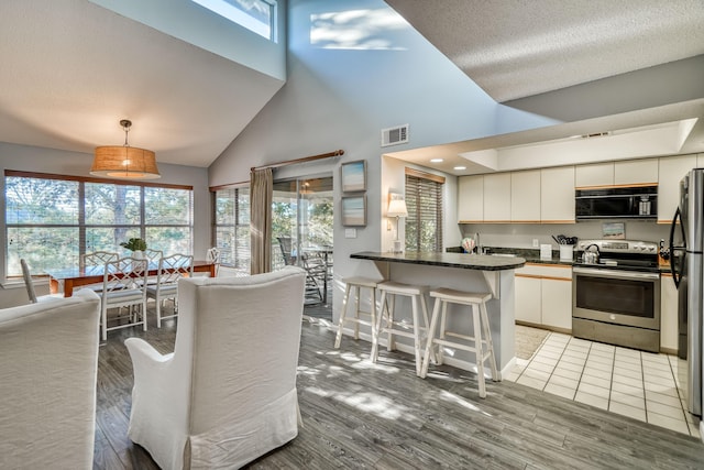 kitchen featuring a breakfast bar, hardwood / wood-style floors, decorative light fixtures, white cabinetry, and stainless steel appliances