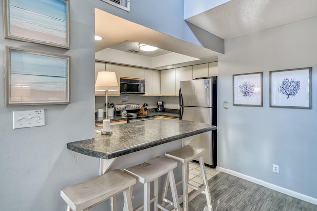 kitchen with a textured ceiling, a kitchen breakfast bar, kitchen peninsula, hardwood / wood-style flooring, and stainless steel appliances