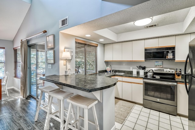 kitchen with sink, white cabinetry, black appliances, a kitchen bar, and kitchen peninsula