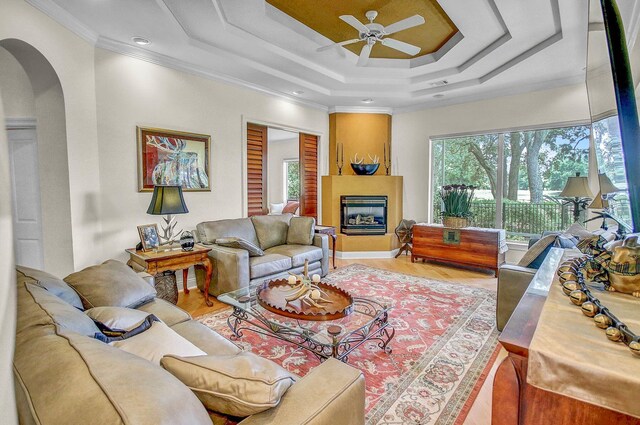 living room featuring a fireplace, wood-type flooring, ceiling fan, a tray ceiling, and ornamental molding