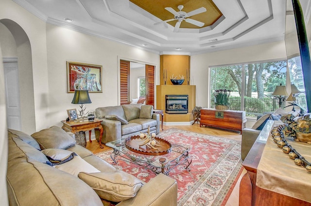 living room with crown molding, a fireplace, a raised ceiling, and hardwood / wood-style floors