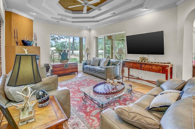 living room featuring hardwood / wood-style flooring, ceiling fan, ornamental molding, and a raised ceiling