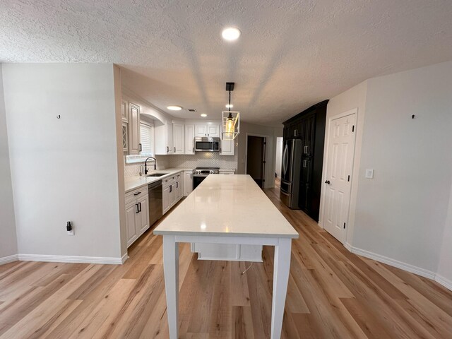 kitchen featuring white cabinetry, stainless steel appliances, light hardwood / wood-style floors, and hanging light fixtures