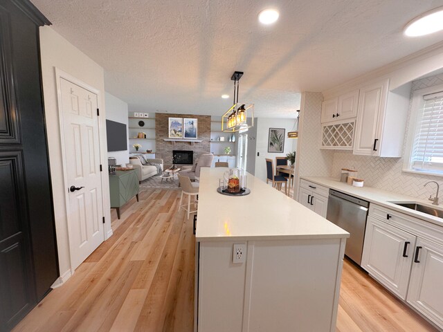 kitchen with sink, dishwasher, white cabinetry, a center island, and a fireplace