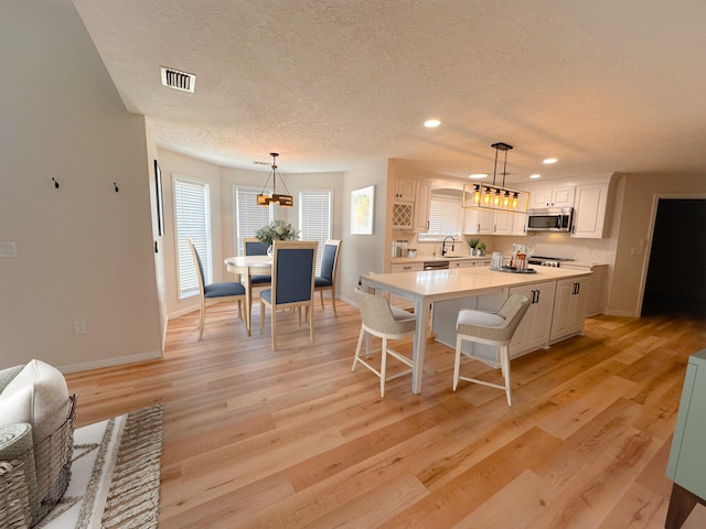 kitchen featuring hanging light fixtures, light hardwood / wood-style flooring, white cabinets, and a kitchen island