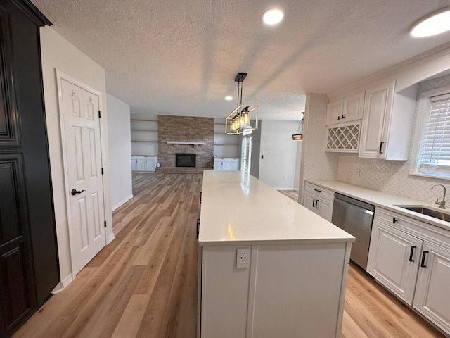 kitchen featuring sink, white cabinetry, a large fireplace, dishwasher, and a kitchen island