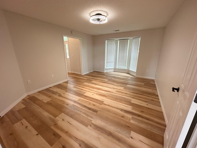 unfurnished bedroom featuring multiple windows, light hardwood / wood-style flooring, and a textured ceiling