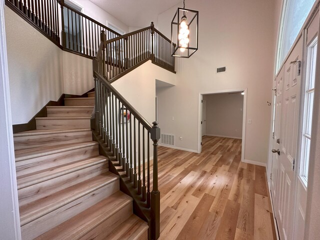 foyer entrance with a notable chandelier, a towering ceiling, and light wood-type flooring