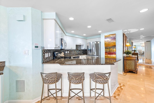 kitchen with a breakfast bar area, dark stone countertops, white cabinets, kitchen peninsula, and stainless steel appliances