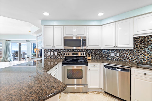 kitchen with white cabinetry, appliances with stainless steel finishes, backsplash, and dark stone counters