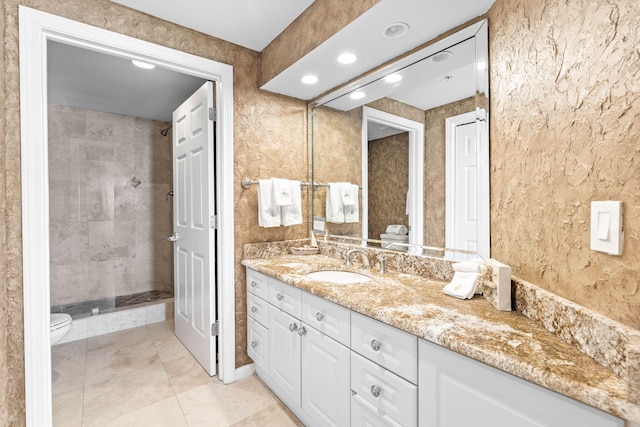 bathroom featuring tile patterned flooring, vanity, a tile shower, and toilet