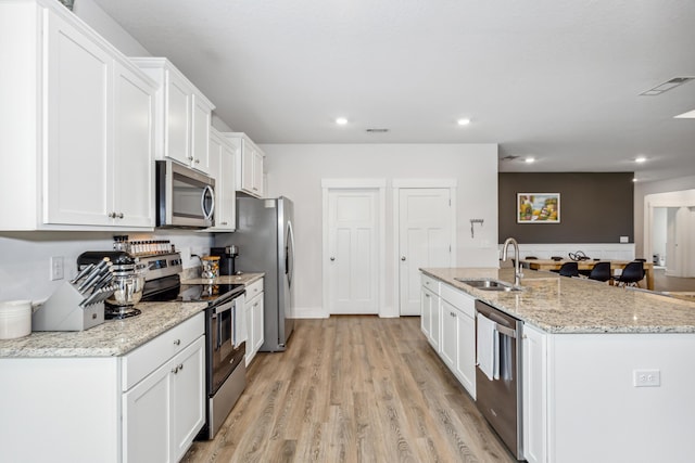 kitchen featuring sink, white cabinetry, light stone counters, appliances with stainless steel finishes, and an island with sink