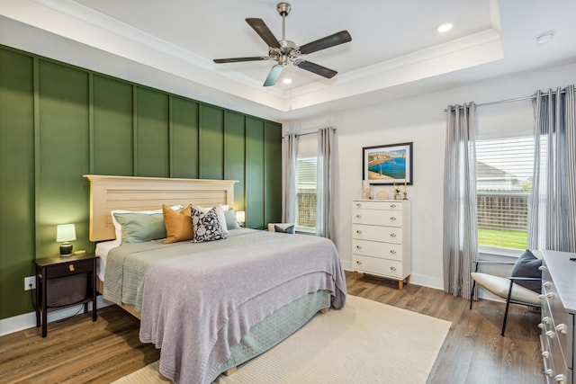 bedroom with hardwood / wood-style flooring, ornamental molding, ceiling fan, and a tray ceiling