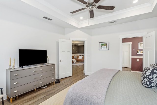 bedroom featuring a raised ceiling, wood-type flooring, ornamental molding, and ceiling fan