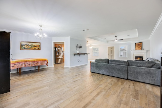 living room featuring ceiling fan with notable chandelier, a raised ceiling, light wood-type flooring, and crown molding