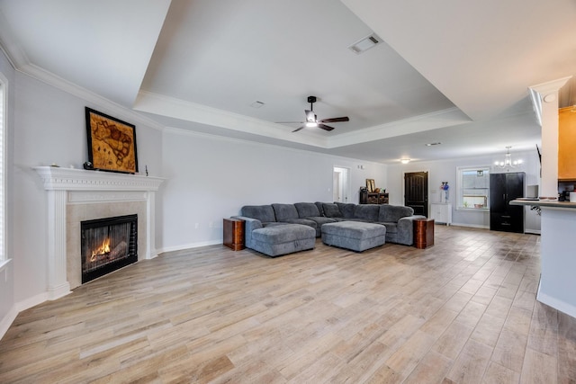 living room featuring ceiling fan with notable chandelier, light hardwood / wood-style floors, a tray ceiling, and crown molding