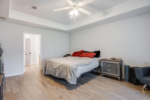 bedroom with light wood-type flooring, ornamental molding, a raised ceiling, and ceiling fan