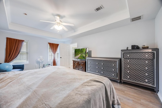 bedroom featuring ceiling fan, light hardwood / wood-style floors, ornamental molding, and a raised ceiling