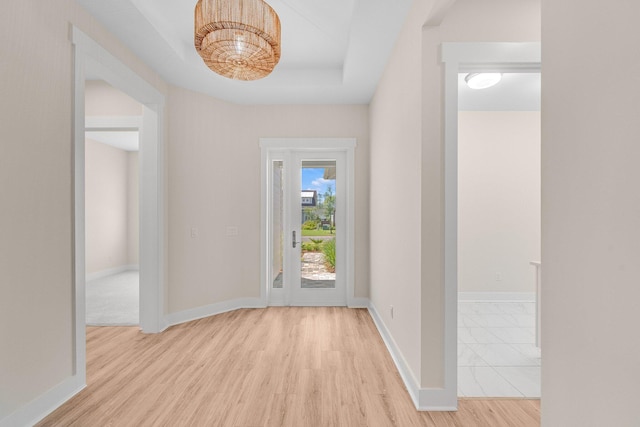 foyer featuring light wood finished floors, baseboards, and a tray ceiling