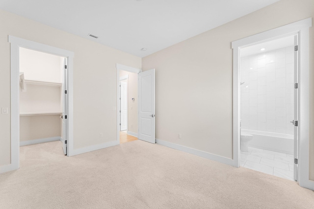 unfurnished bedroom featuring a closet, visible vents, a spacious closet, light carpet, and baseboards