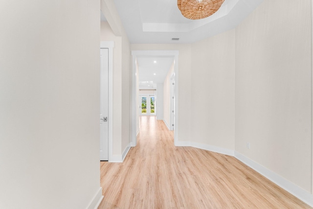 hall featuring light wood-style floors, baseboards, and a raised ceiling