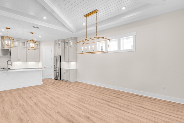 kitchen featuring stainless steel fridge, tasteful backsplash, glass insert cabinets, hanging light fixtures, and light countertops