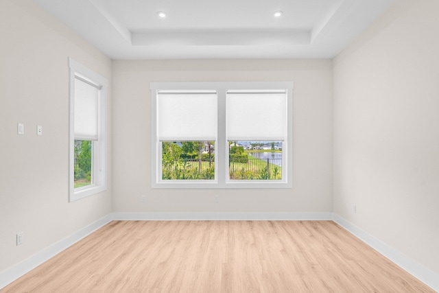 spare room featuring a tray ceiling, light wood-type flooring, and baseboards