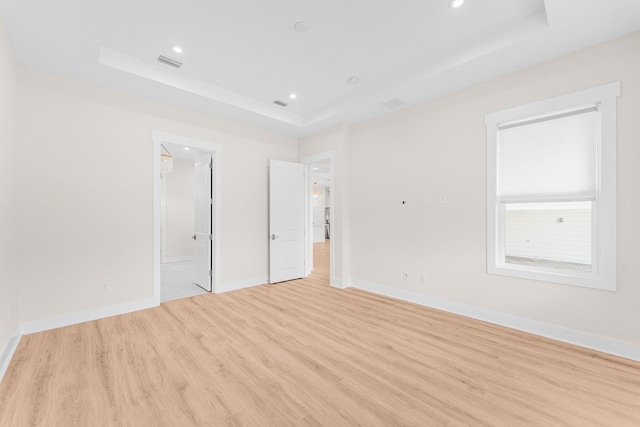 unfurnished room featuring baseboards, a tray ceiling, visible vents, and light wood-style floors