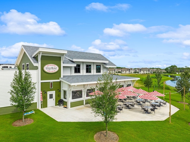 back of house with a patio, a yard, roof with shingles, and a water view