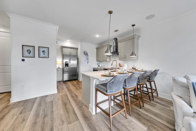 kitchen featuring wall chimney exhaust hood, a breakfast bar, built in refrigerator, gray cabinets, and pendant lighting