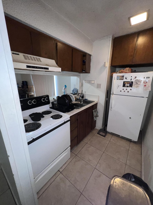 kitchen with dark brown cabinetry, sink, white appliances, and light tile patterned flooring