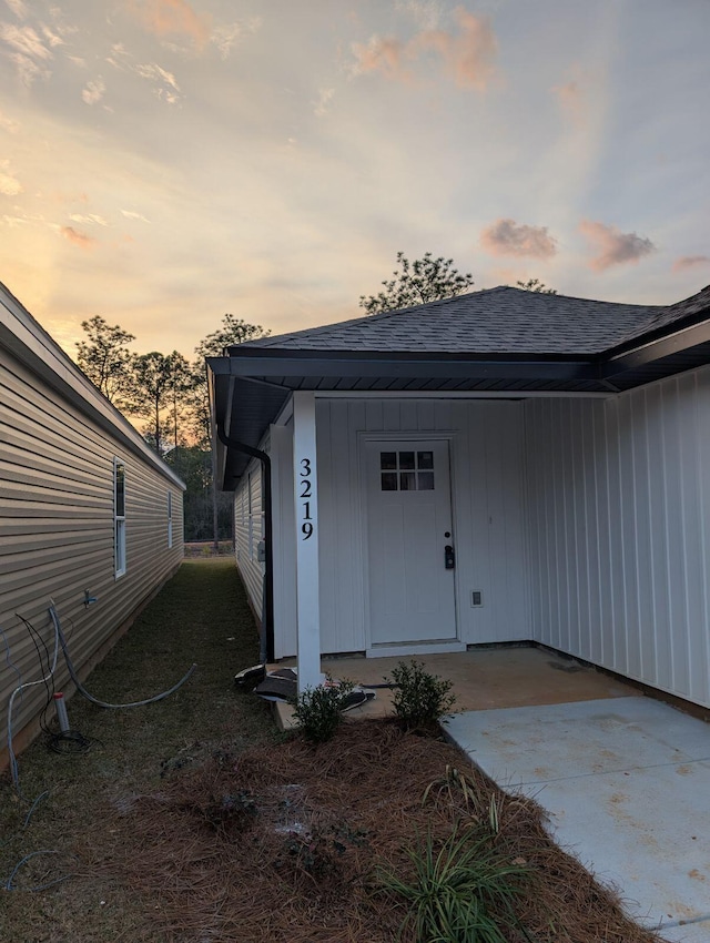 view of exterior entry with board and batten siding and a shingled roof