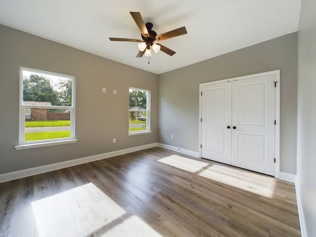 unfurnished bedroom with a ceiling fan, a closet, baseboards, and wood finished floors